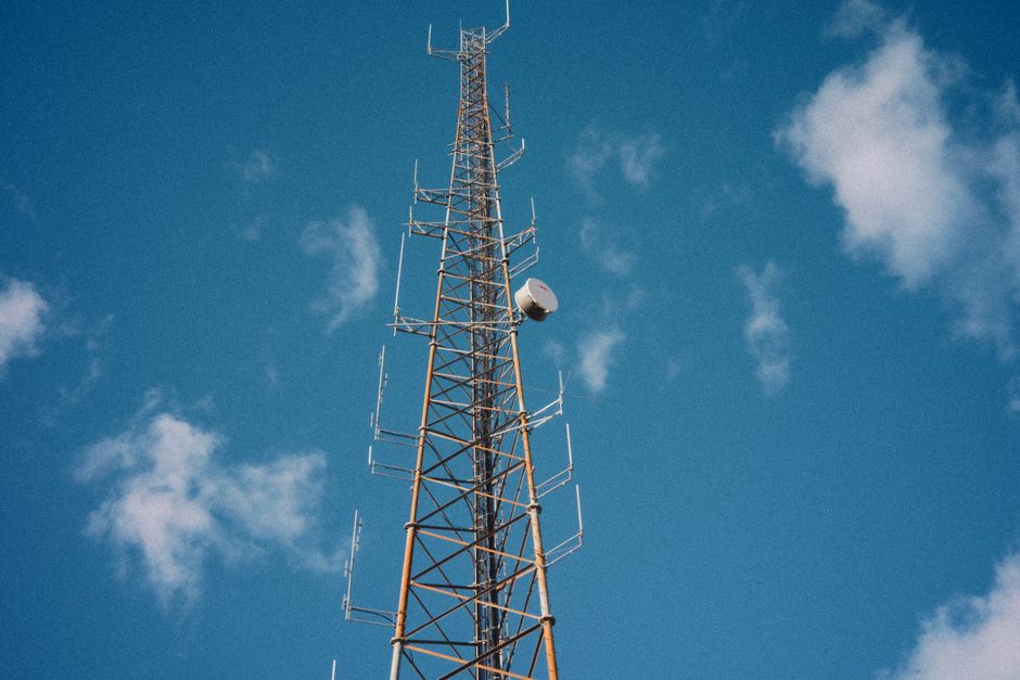 Vertical communication tower reaching into a bright blue sky with scattered clouds.